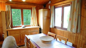 Una cabaña de madera con una mesa de comedor, sillas y un ventanal con cortinas.