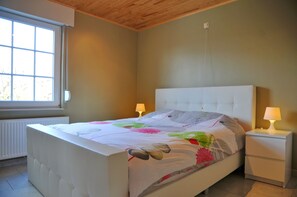 A bedroom with a bed, two bedside lamps, a window, and a radiator. - Bonheur (Somme-Leuze)
