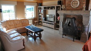 A living room with a leather sofa, a wooden coffee table, a fireplace, a television, and a brick wall.