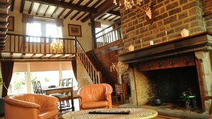 A cozy room with a fireplace, leather chairs, a table, and a staircase leading to an upper level. - Bourrasques (Marche-en-Famenne)