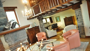 A cozy living room with a stone fireplace, leather chairs, a television, and a chandelier. - Bourrasques (Marche-en-Famenne)