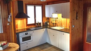 Een kleine keuken met houten wanden, een zwarte afzuigkap, witte kastjes, een spoelbak en een tafeltje met fruit.