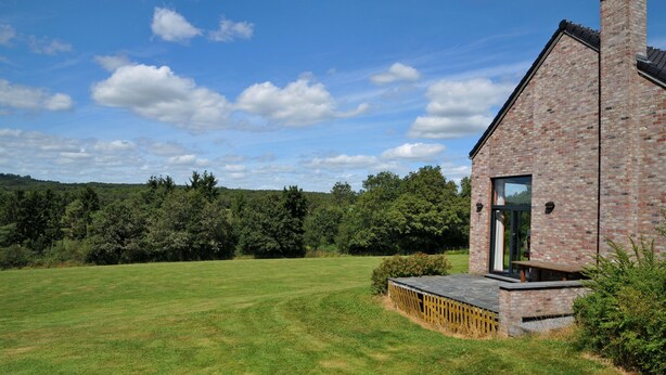 Une maison en briques avec une grande pelouse et une terrasse en bois.