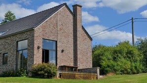Une maison moderne en briques, dotée de grandes fenêtres et d’une cheminée.