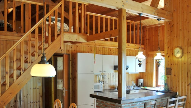 A wooden interior with a dining area, leather sofa, kitchen, and staircase.