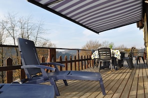 A wooden deck with lounge chairs and a table, overlooking a mountainous landscape.