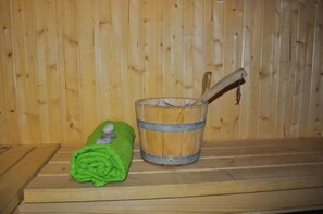 A wooden bench with a green towel and a wooden bucket with a wooden mallet.