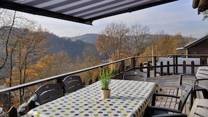 Ein überdachter Sitzbereich mit Tisch und Stühlen, mit Blick auf eine gebirgige Landschaft.