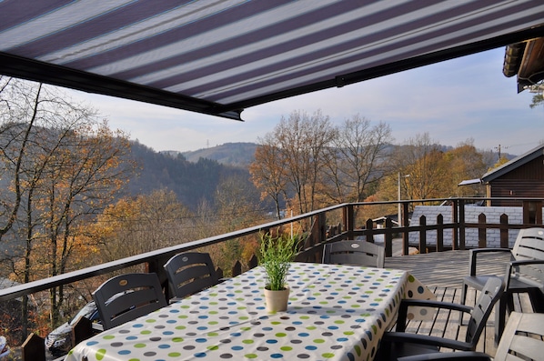 A covered outdoor seating area with a table and chairs, overlooking a mountainous landscape.