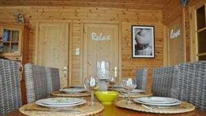 Ein Holzblockhaus-Interieur mit einem Esstisch, gedeckt für vier Personen, umgeben von Korbstühlen.