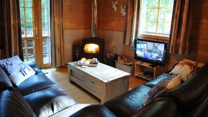A cozy living room with a fireplace, leather sofas, a television, and a wooden interior. - Chalet Mady (Erezee)