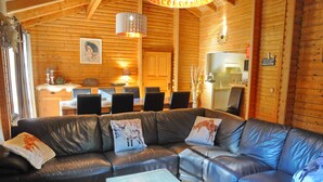 A cozy log cabin interior with a leather sofa, dining table, and kitchen area. - Chalet Mady (Erezee)