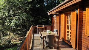 A wooden deck with a table and chairs, surrounded by dense trees. - Chalet Mady (Erezee)