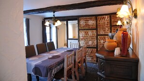 A dining area with a table set for four, wooden chairs, a brick wall, and a wooden cabinet with a vase and salt shakers. - Chard'heureux (Somme-Leuze)