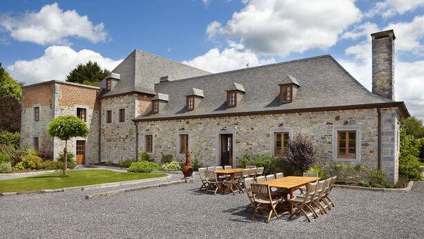 Un bâtiment en pierre avec une allée gravillonnée et un espace extérieur aménagé pour s’asseoir.