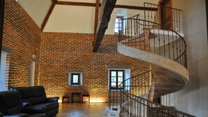 Une pièce spacieuse avec un mur en briques, un escalier en colimaçon et un coin salon comprenant un canapé et une table.