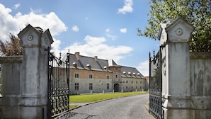 Un bâtiment historique avec une allée de gravier menant à une entrée fermée par un portail.