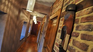 Un couloir étroit avec un plancher en bois et un mur en briques. On y trouve plusieurs portes et un luminaire suspendu.