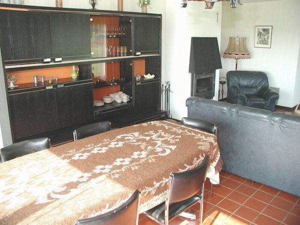 Un comedor con una mesa cubierta por un mantel estampado, rodeada de sillas. Se observa un sofá y una silla al fondo.