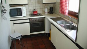 A compact kitchen with white cabinets, a microwave, a red kettle, a coffee maker, and a sink. - Chenets 'Les Hirondelles' (Bievre)