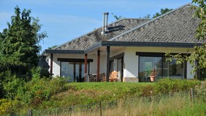 A modern house with a stone roof, large windows, and a covered patio area with outdoor furniture. - Chevalerie (Somme-Leuze)