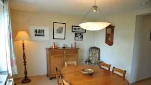 A dining area with a wooden table, chairs, a lamp, a cabinet, and framed pictures on the wall. - Clef des Champs (Somme-Leuze)