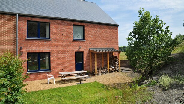 A brick house with a covered porch, a picnic table, and a stack of firewood. - Clef des Champs (Somme-Leuze)