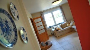 A living room with a sofa, a wooden door, and a window with curtains. - Clef des Champs (Somme-Leuze)
