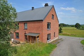 Situated on a rural road, this traditional house offers a peaceful countryside view and a welcoming front porch with a bench and table.