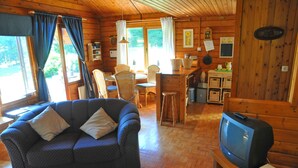Un acogedor interior de cabaña con sofá, televisor, zona de comedor y paredes de madera.