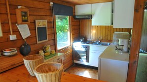 Una cocina estilo cabaña con paredes de madera, estufa, fregadero y refrigerador. Hay cestas sobre la mesa y una ventana con vista a la vegetación exterior.