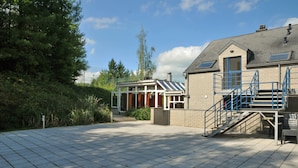 A building with a covered patio area, a staircase with blue railings, and a brick exterior. - Ecureuil (Durbuy)