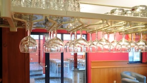 A restaurant interior with hanging wine glasses, a wooden counter, and a view of the outdoor seating area. - Ecureuil (Durbuy)