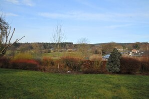 A rural landscape with a grassy field, a small tree, and a distant view of houses and trees.