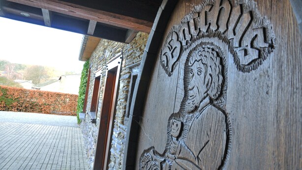 A carved wooden panel with a figure and text, part of a building's exterior. - Fermette Arbrefontaine (Lierneux)