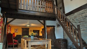 A wooden staircase with a stone wall, a dining area with a table and chairs, and a red chair. - Fermette Arbrefontaine (Lierneux)