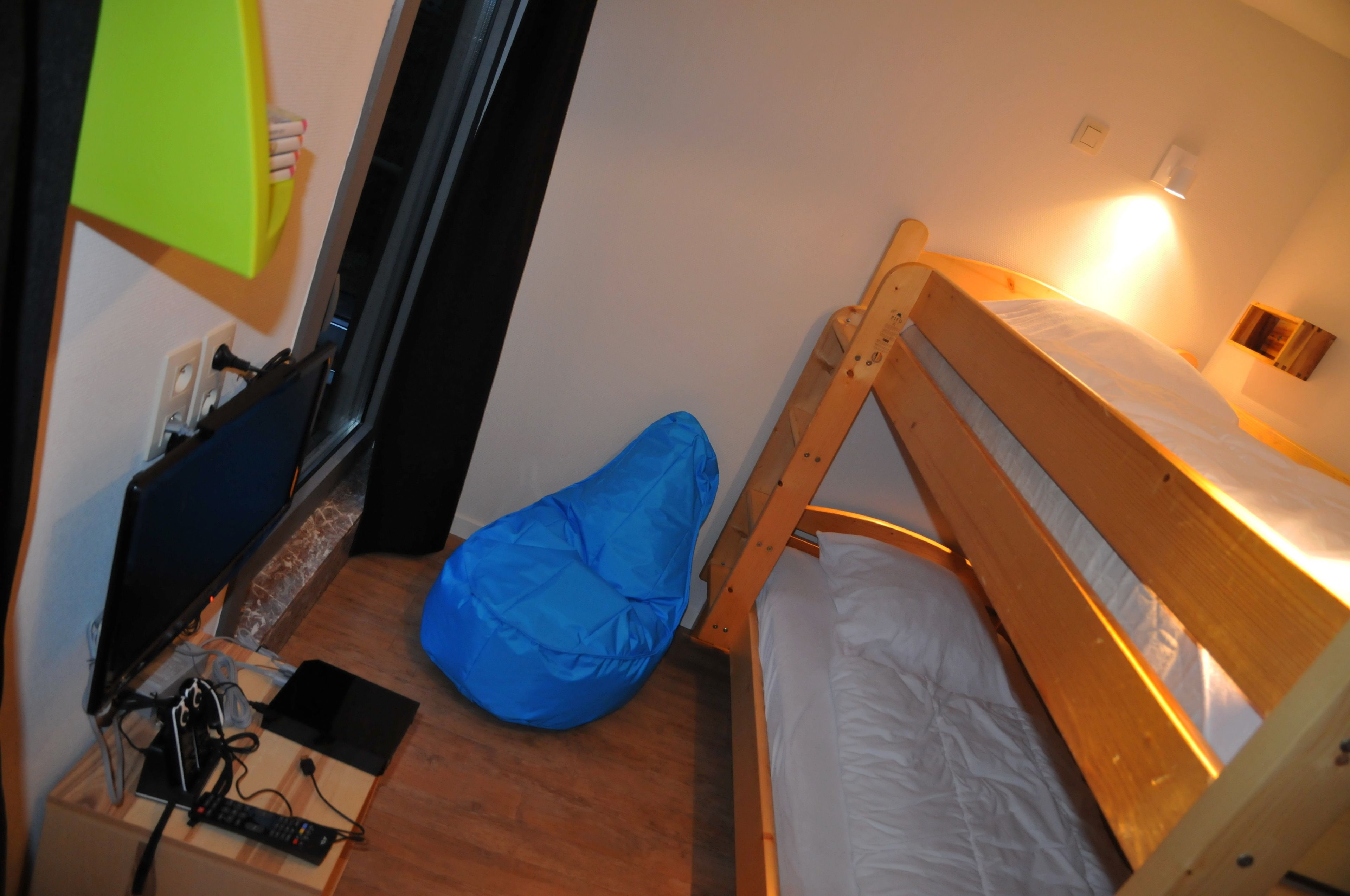 Une petite pièce avec un lit superposé, un bureau avec un ordinateur et un fauteuil en forme de poire de couleur bleue.