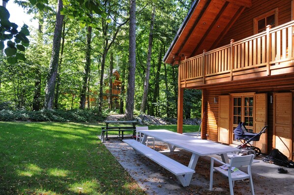 A wooden cabin with a picnic table and benches, surrounded by a forest.