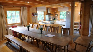 Una cabaña de madera con una gran mesa de comedor, bancos y una zona de cocina con estufa, fregadero y refrigerador.