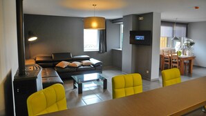 A modern living room with a sofa, yellow chairs, a coffee table, a TV, and a dining area with a table and chairs.