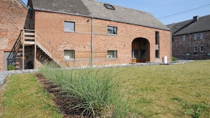 A brick building with a wooden staircase leading to a door, a large arched entrance, and a small window.
