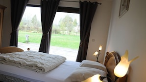 Una cama bien hecha con un colchón acolchado, una lámpara de noche y vistas a un césped verde a través de una ventana con cortinas.