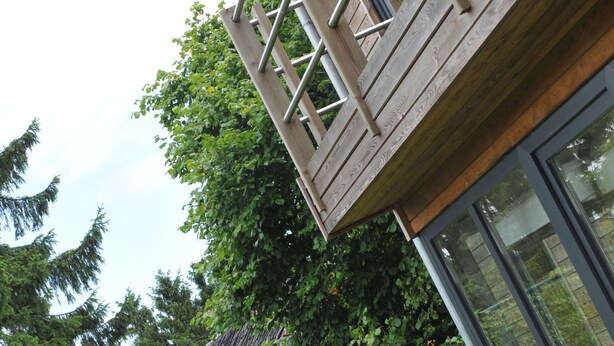 Un edificio moderno con fachada de madera, ventanas amplias y barandilla de metal en el balcón.