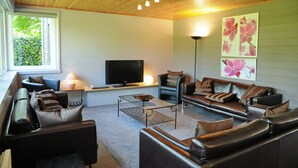 Una sala de estar moderna con una televisión de pantalla plana, sofás de cuero, una mesa de centro y un amplio ventanal.