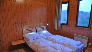A wooden-paneled room with a bed, a small table, and a window with a view of trees. - Jardins de l'Ourthe 16 (Houffalize)