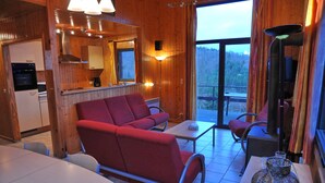 A cozy cabin interior with a dining area, a sofa, a table, and a kitchen. - Jardins de l'Ourthe 16 (Houffalize)