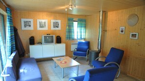 Une pièce comprenant un canapé, deux fauteuils bleus, une petite table, un téléviseur et un radiateur.