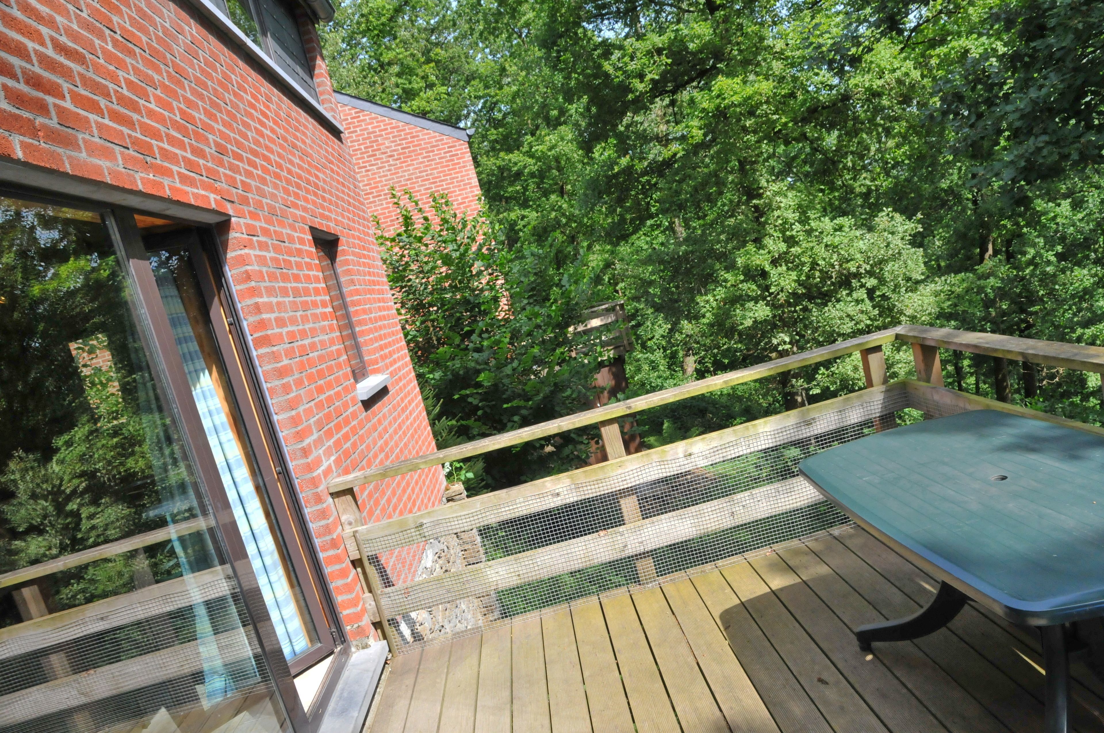 En træterrasse med et bord og stole, omgivet af en murstensmur og frodig vegetation.
