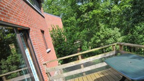Une terrasse en bois avec une table et des chaises, entourée d’un mur de briques et d’une végétation luxuriante.