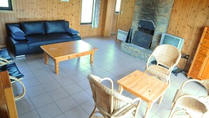 A cozy room with a wooden sofa, a wooden coffee table, wicker chairs, a stone fireplace, and a television. - Kangourou 2 (Hastiere)
